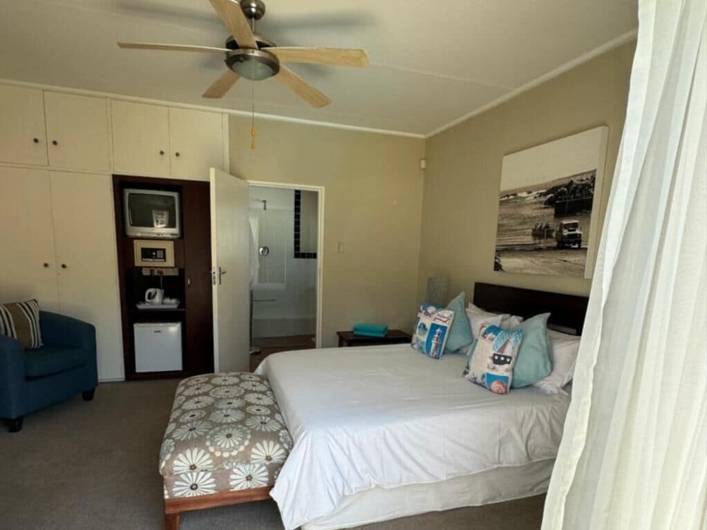 A bedroom with a bed, a ceiling fan, a television, a desk, and a wardrobe.