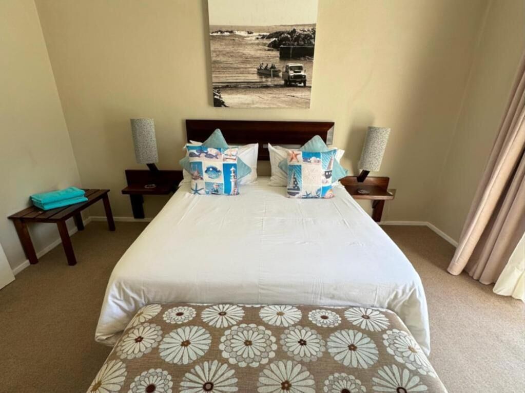 A hotel room with a large bed, two bedside tables, a headboard, and a wall-mounted picture.