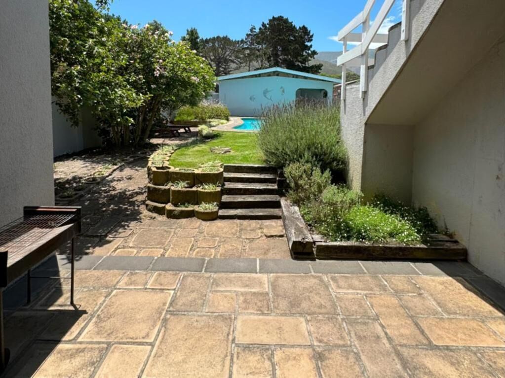 Un patio con piso de piedra, una piscina y un edificio azul claro al fondo.
