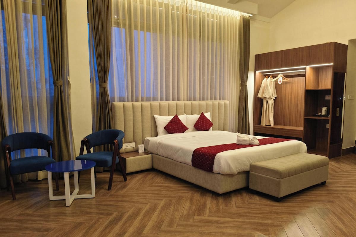 A hotel room with a large bed, two chairs, a small table, a wardrobe, and a mirror.