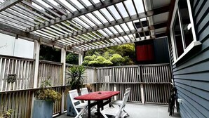 An outdoor patio with a wooden pergola, a red table, and white chairs. - Botanic Garden Retreat | Sleeps 6 | 3 Ensuite Bedrooms (Wellington)