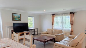A living room with a television, sofa, coffee table, and a painting on the wall. - Botanic Garden Retreat | Sleeps 6 | 3 Ensuite Bedrooms (Wellington)