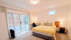 A bedroom with a bed, a desk, a chair, a small table, and a window. - Botanic Garden Retreat | Sleeps 6 | 3 Ensuite Bedrooms (Wellington)