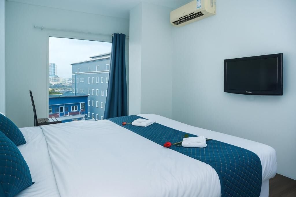 Une chambre d’hôtel équipée d’un lit, d’un téléviseur à écran plat, d’un système de climatisation et d’une fenêtre donnant sur des immeubles.