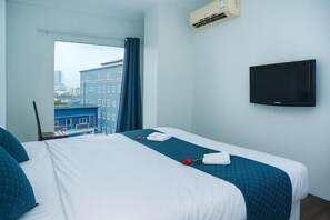Hotelkamer met een bed, een flatscreen-tv, een airconditioning en een raam met uitzicht op gebouwen.