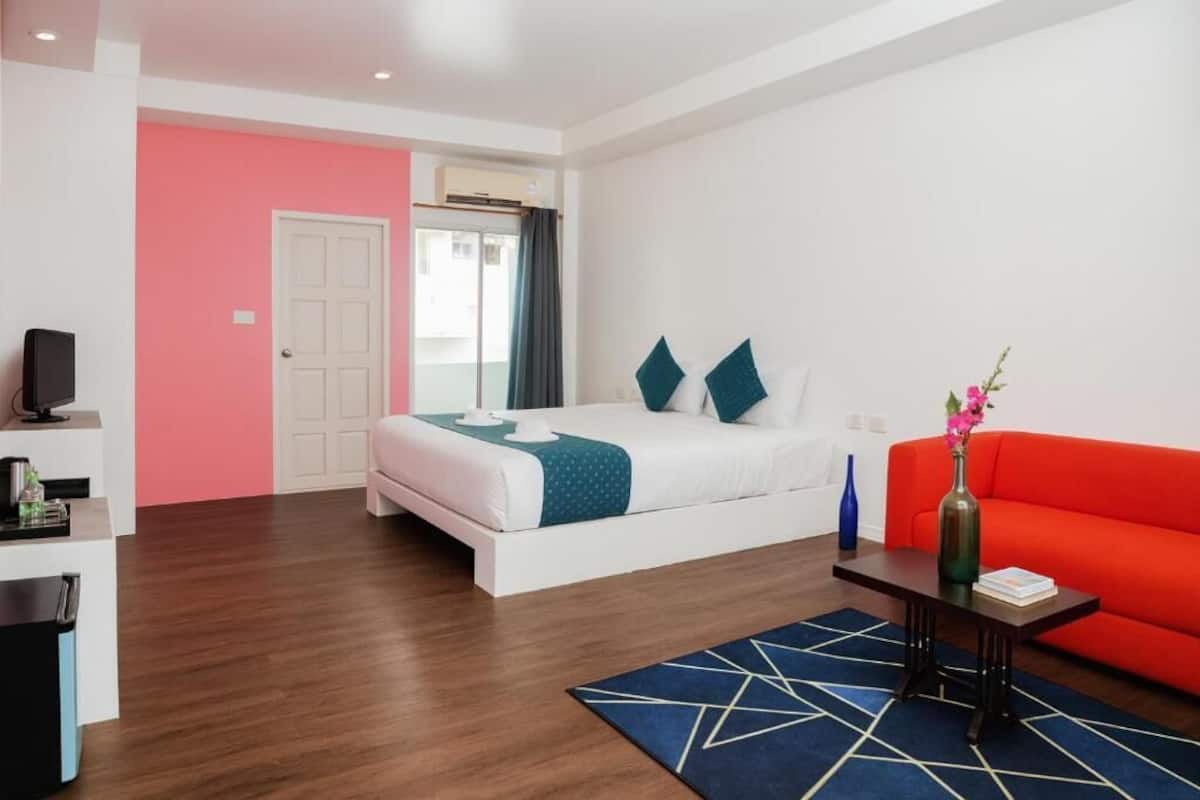 A hotel room with a bed, a red sofa, a small table with a vase, and a TV on a stand.