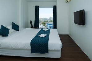 Een hotelkamer met een bed, een televisie, een raam met gordijnen en uitzicht op gebouwen.