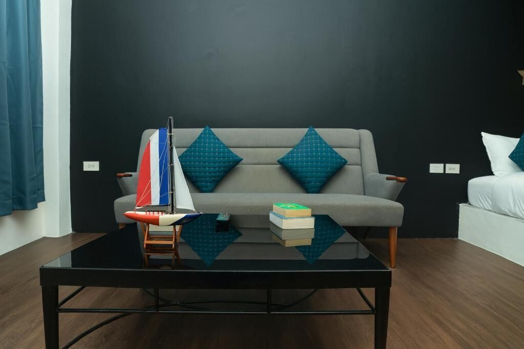 A modern room with a grey sofa, teal pillows, a small sailboat model, and a stack of books on a glass coffee table.