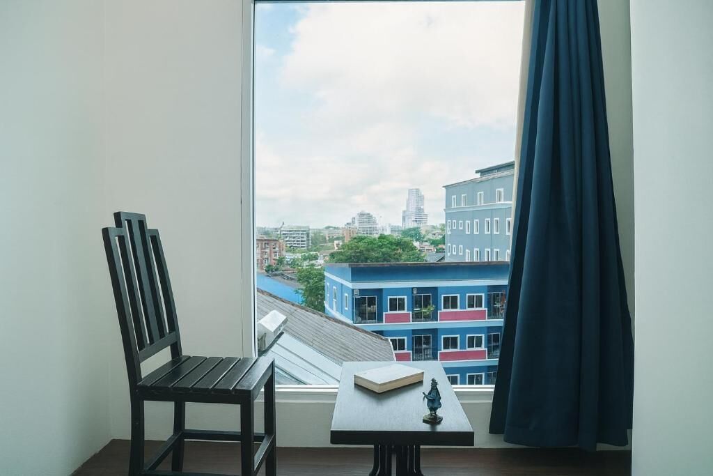 A room with a view of a cityscape, a chair, a table with a book and a statue, and a curtain.