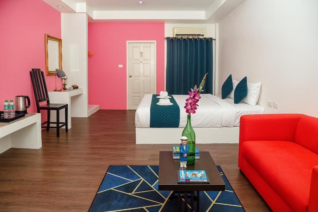 A hotel room with a bed, a red sofa, a desk with a chair, a coffee table, and a mirror.