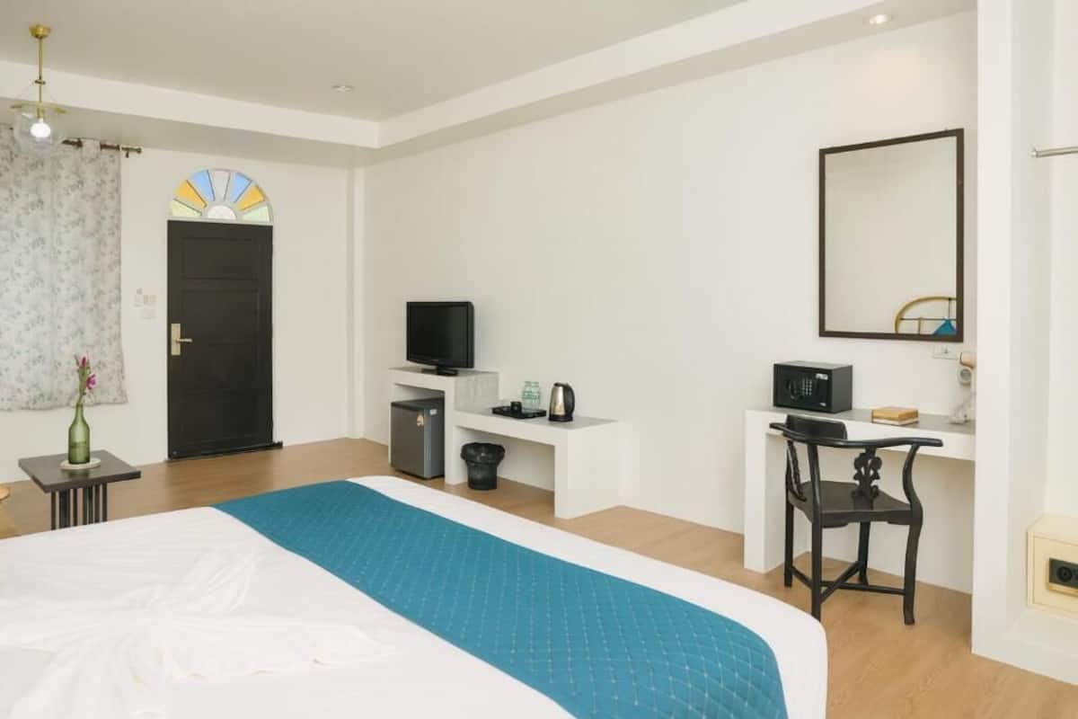 A hotel room with a bed, a desk with a chair, a television, a small refrigerator, and a mirror on the wall.