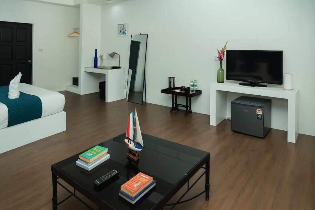 Ein modernes Hotelzimmer mit einem Bett, einem Fernseher, einer kleinen Kühlbox, einer Kaffeemaschine und einem Schreibtisch mit Computer und Büchern.