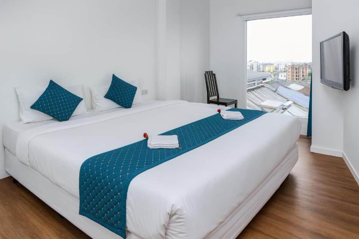 A hotel room with a large bed, a TV mounted on the wall, and a city view through the window.