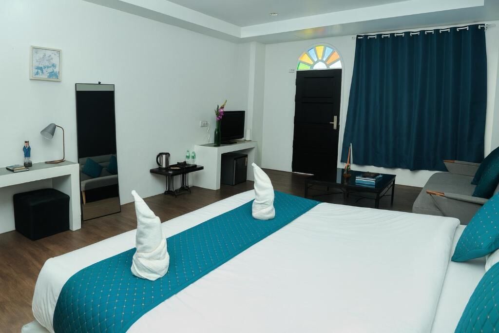 A hotel room with a bed, a desk, a chair, a TV, and a window with curtains.