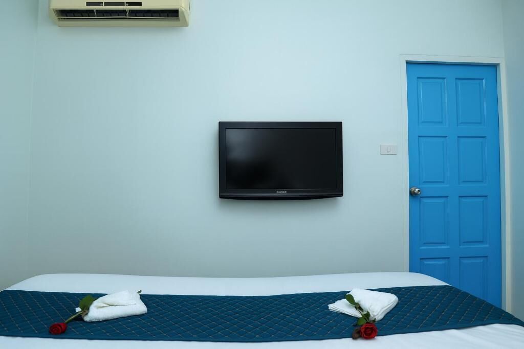 A hotel room with a bed, a television mounted on the wall, and a blue door.