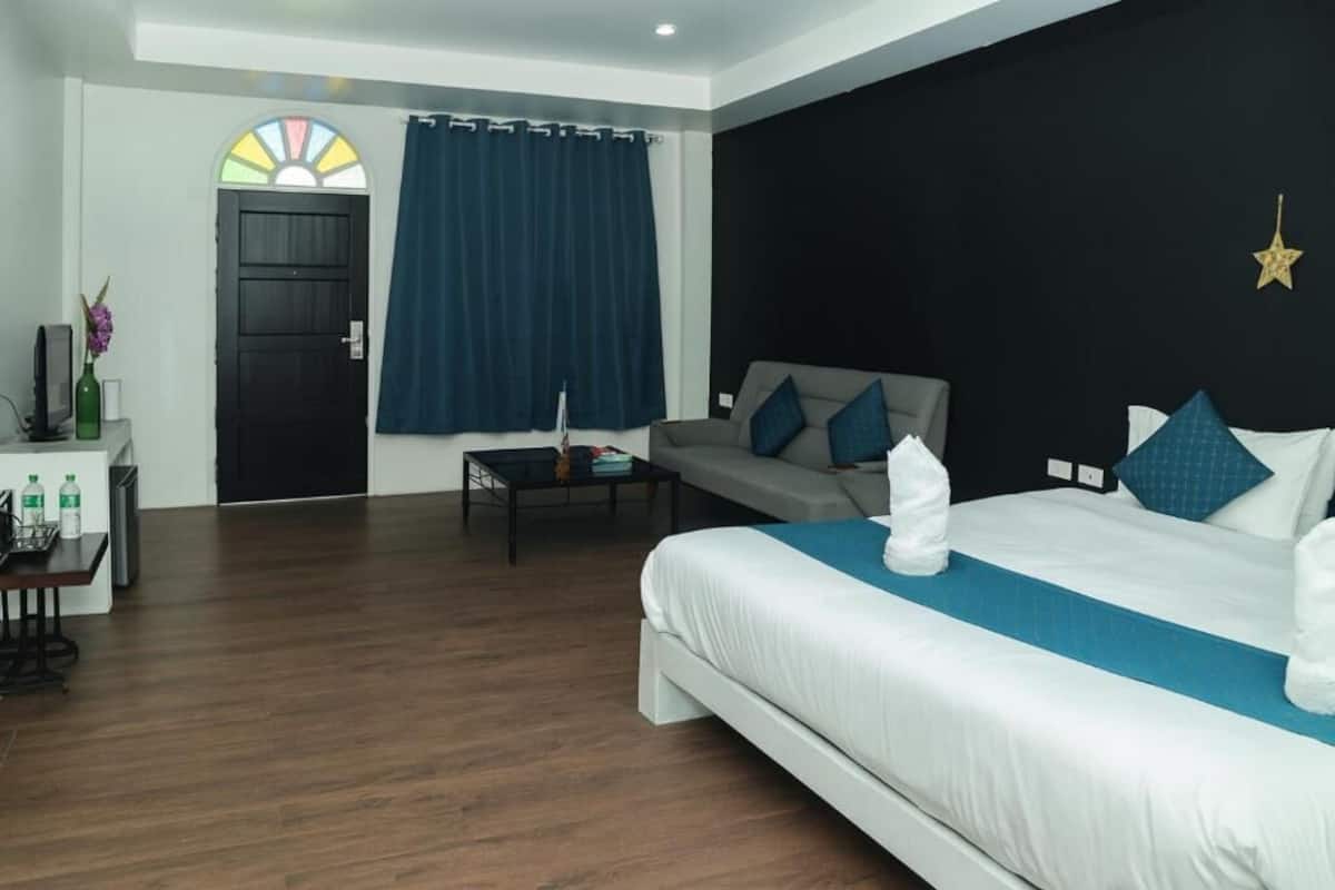 A hotel room with a bed, a sofa, a desk, and a window with curtains.