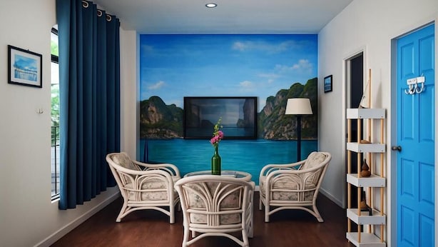 Une pièce avec vue sur une mer bleue et des falaises, une table ronde avec des chaises, un téléviseur et une porte bleue.