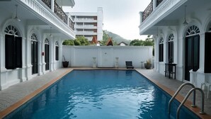 Une piscine à l’extérieur blanc, entourée d’un mur blanc et dotée d’un balcon avec des rampes noires.
