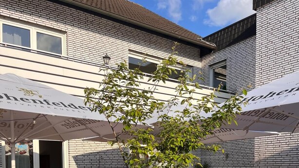 A patio area with outdoor seating, a small tree, and a brick planter. - Hillerts Hotel (Rheda-Wiedenbrück)