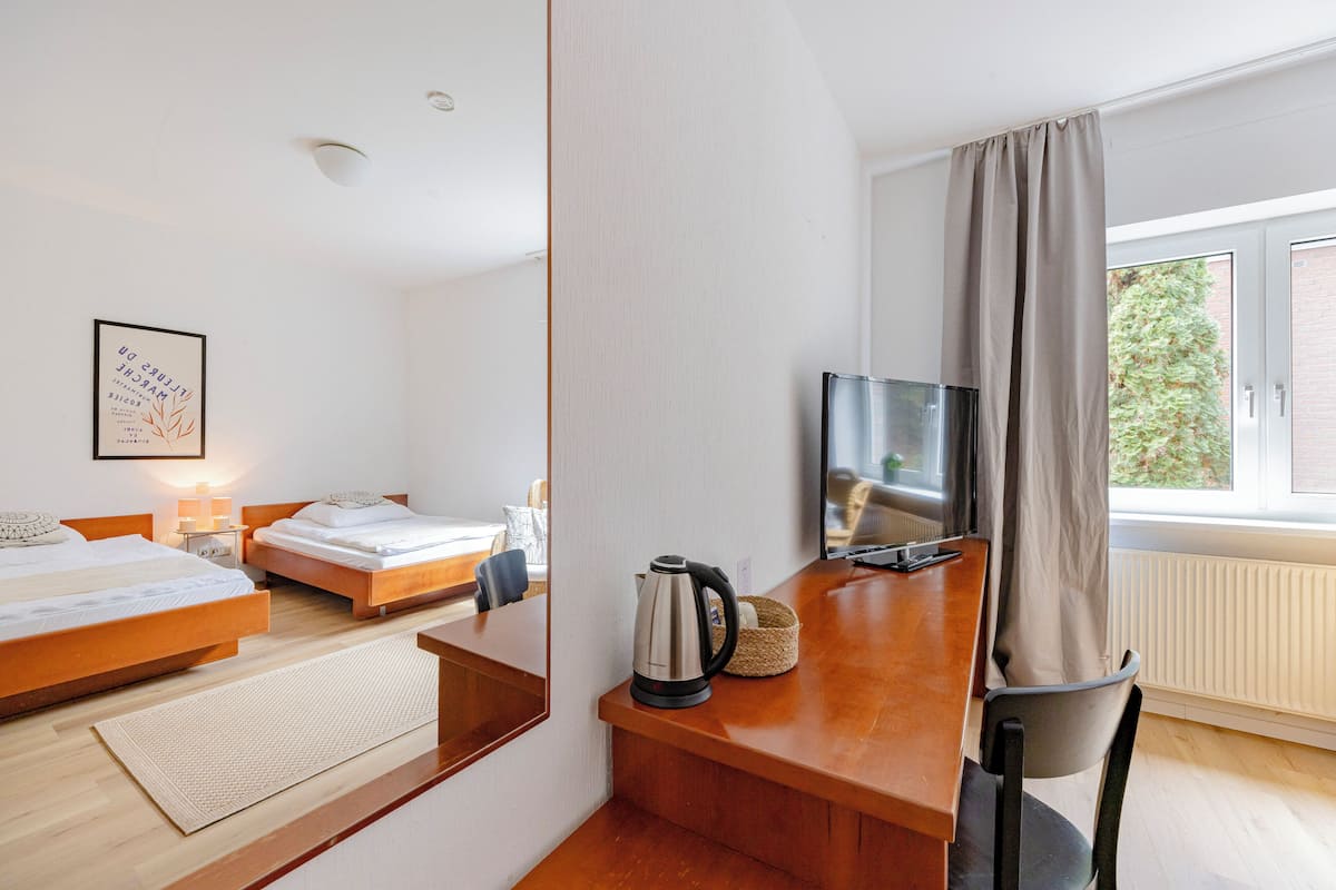 Habitación de hotel con dos camas, un escritorio con hervidor, televisión y vistas a zonas verdes.