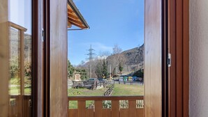 Une porte à ossature en bois qui donne sur un balcon offrant une vue sur une zone herbeuse, une clôture et une montagne en arrière-plan.