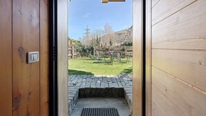 Une porte en bois donne sur une cour intérieure où se trouvent un banc en pierre, une grille en métal et, au fond, une clôture en bois.