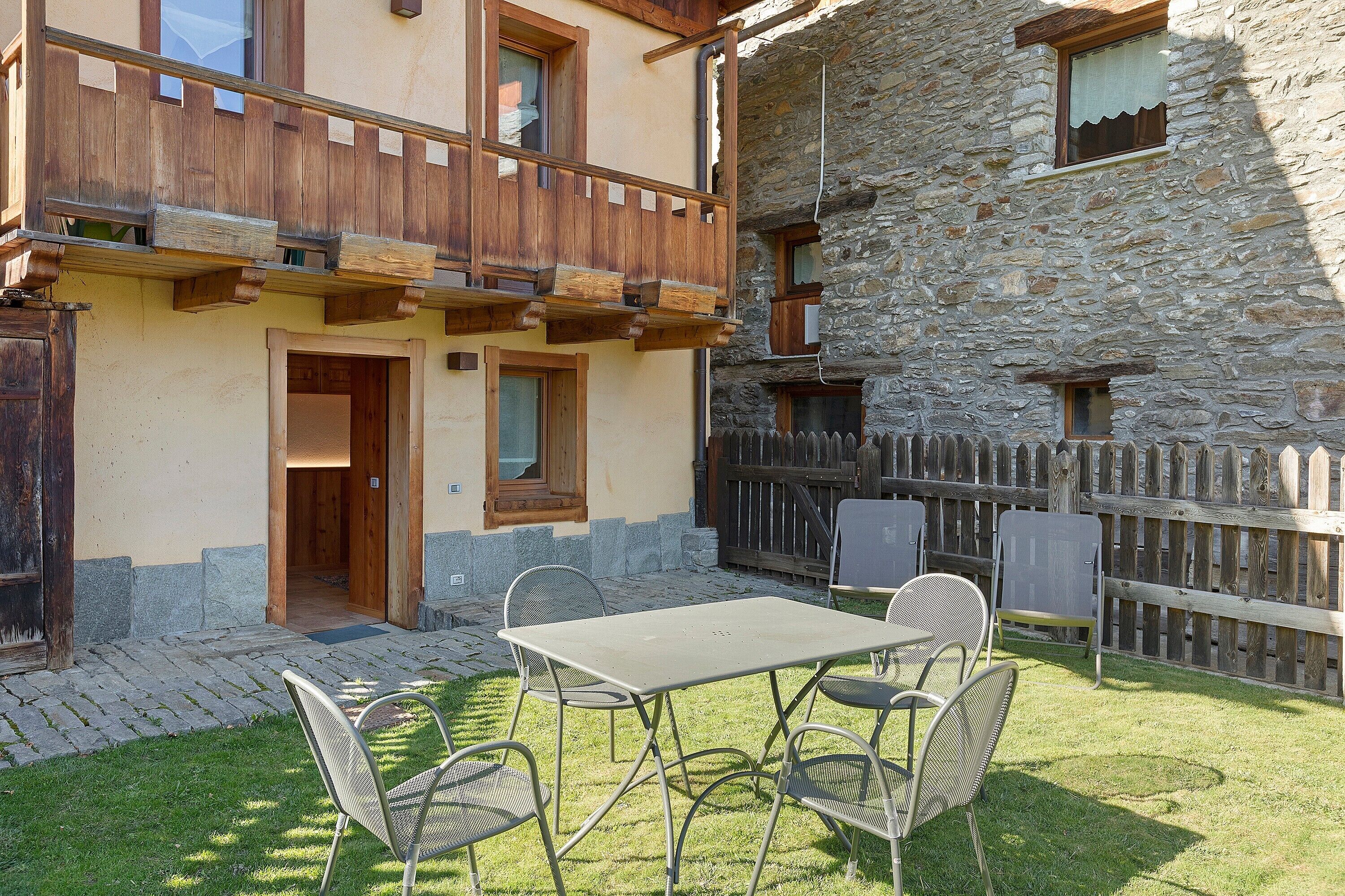 Un bâtiment en pierre doté d’un balcon, d’une porte en bois et d’une table avec des chaises dans la cour.