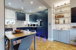 Una cocina moderna con armarios azul oscuro, una mesa de comedor de madera y una estantería empotrada con diversos objetos.