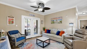 A living room with a ceiling fan, a sofa, a chair, a coffee table, and a door with glass panels. - Travel Ball-Travel Nurses-OWA-9.7 miles To Beach (Foley)