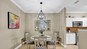 A dining area with a round table, chairs, a chandelier, and a colorful abstract painting on the wall. - Travel Ball-Travel Nurses-OWA-9.7 miles To Beach (Foley)