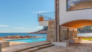 Une maison moderne avec une piscine, des piliers en pierre et une vue sur la mer.