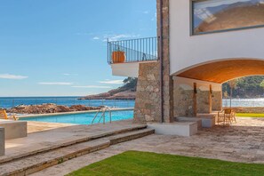 Ein modernes Haus mit Pool, Steinsäulen und Meerblick.