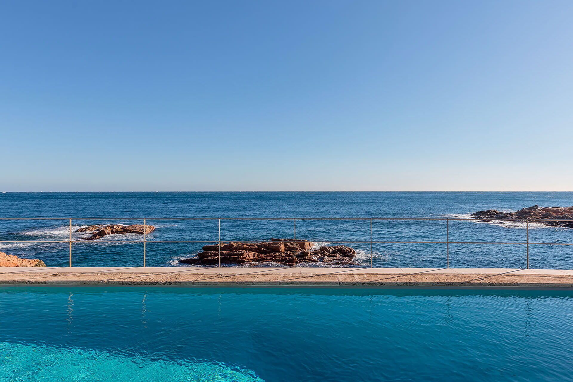 Una piscina azul cristalina con vista al océano y formaciones rocosas.
