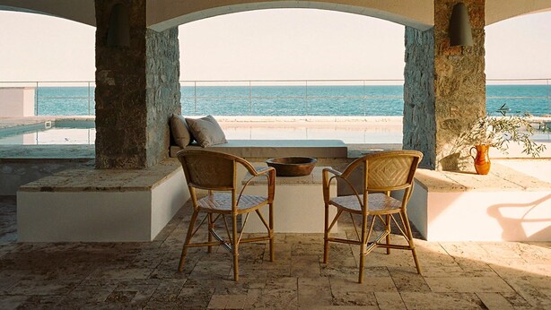 Une terrasse avec deux fauteuils en osier, un mur en pierre et une vue sur la mer.