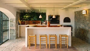 Une cuisine dotée d’un îlot central en pierre, de chaises en bois, de luminaires suspendus et d’une cheminée.