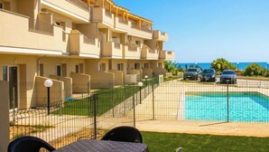 Un edificio de varios pisos con balcones, una piscina y coches aparcados.