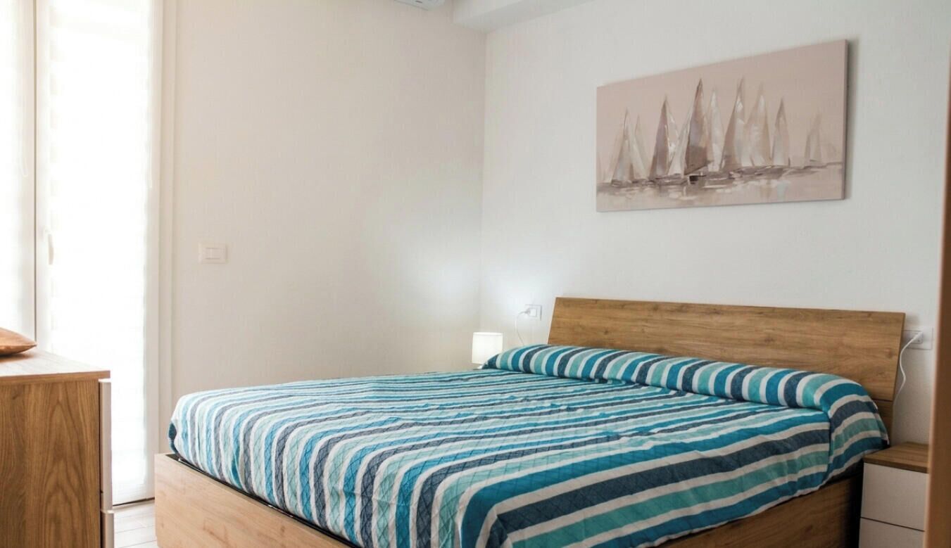 Een slaapkamer met een bed, een houten hoofdbord, een nachtkastje, een bedtafel, een lamp en een wanddecoratie.