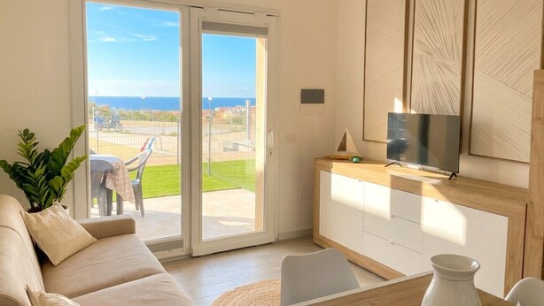 Una sala de estar moderna con un sofá, un televisor y una puerta corrediza de vidrio que da a un balcón.