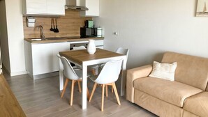 Un espacio habitable compacto con kitchenette, una mesa de comedor con sillas y un sofá.