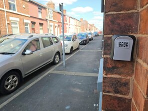 A street with parked cars and a brick wall with a keypad on it. - 3-Bedroom Town Centre House | Sleeps 8 | Self Check-in | Parking | Pet Friendly (St Helens)