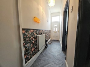 En gang med tapet med mønster, en radiator og en dør for enden.
