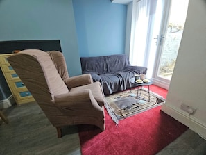 A room with a blue wall, a brown chair, a grey sofa, a small round table with two cups, and a red carpet. - 3-Bedroom Town Centre House | Sleeps 8 | Self Check-in | Parking | Pet Friendly (St Helens)