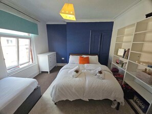 A bedroom with a bed, a nightstand, a dresser, a window, and a bookshelf. - 3-Bedroom Town Centre House | Sleeps 8 | Self Check-in | Parking | Pet Friendly (St Helens)
