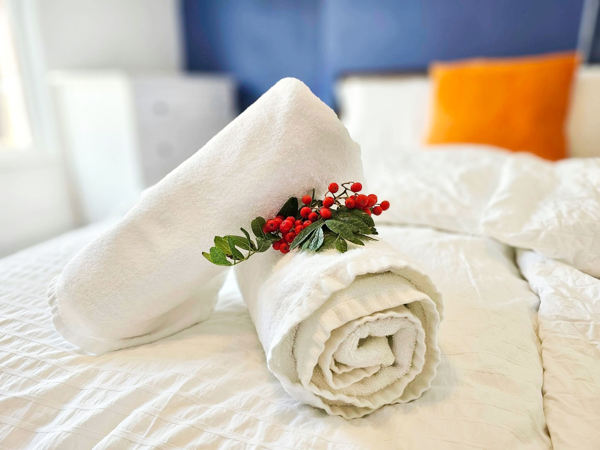 Ein ordentlich gefaltetes Handtuch mit einer dekorativen Anordnung aus Blättern und Beeren auf einem Bett mit einer gesteppten Musterung.