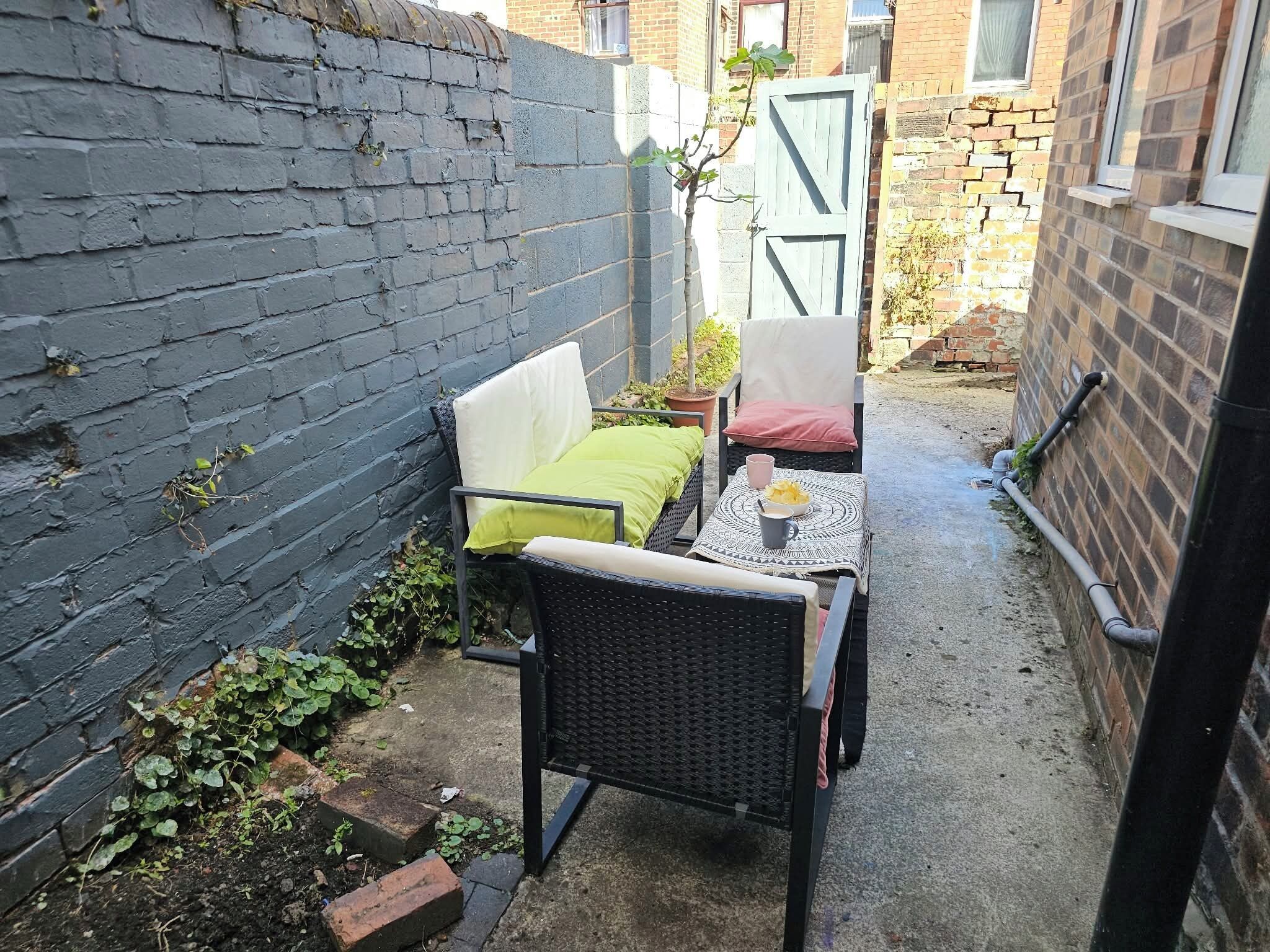 Un espacio exterior reducido con una zona de estar que incluye una silla de mimbre y una mesita con una taza y un plato.