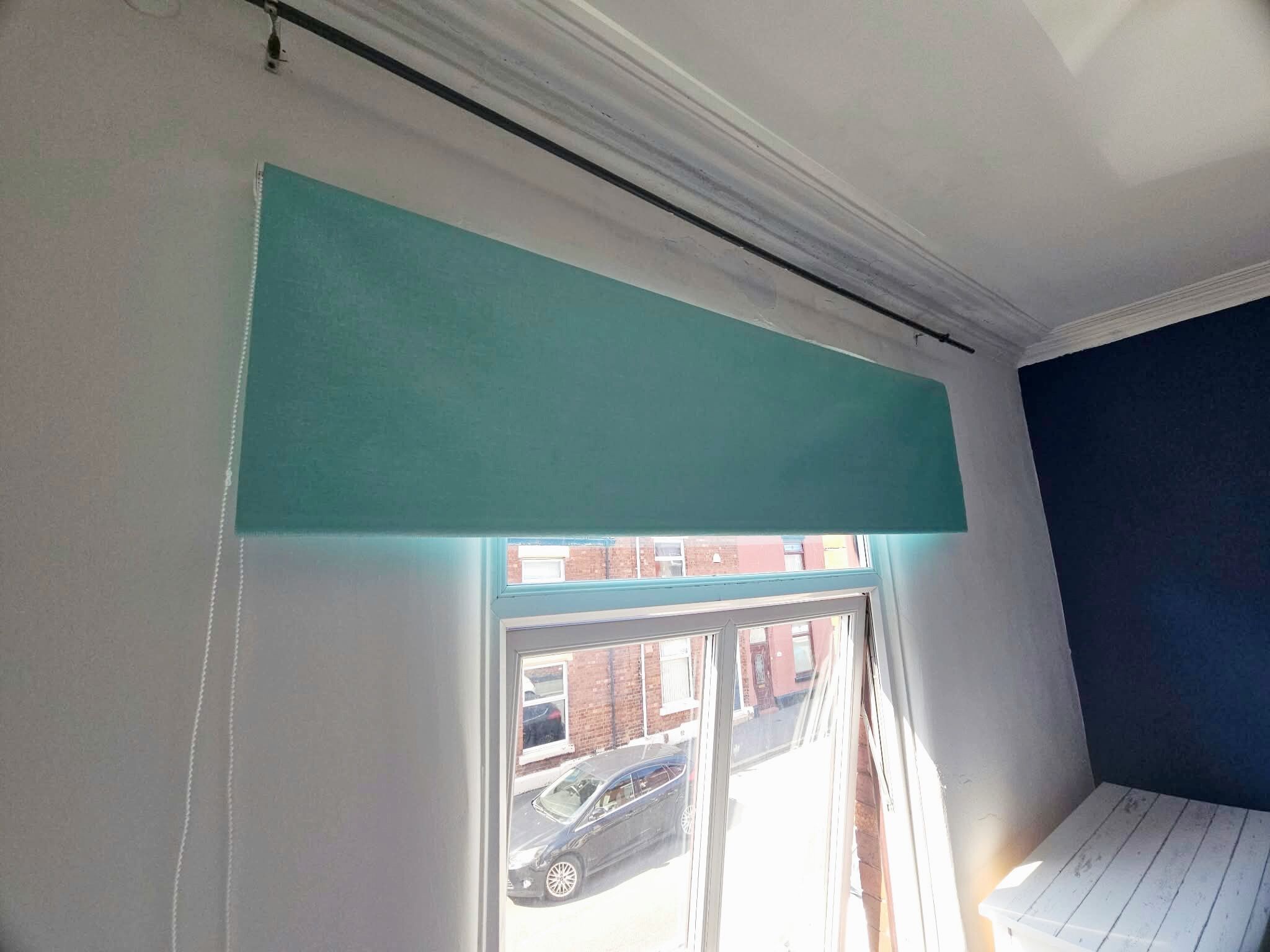 Una habitación con ventana, pared color turquesa y techo blanco.