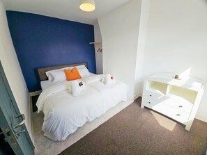 A hotel room with a bed, a nightstand, a dresser, and a blue accent wall. - 3-Bedroom Town Centre House | Sleeps 8 | Self Check-in | Parking | Pet Friendly (St Helens)