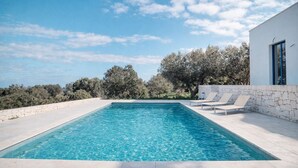 A rectangular swimming pool with clear blue water, surrounded by a stone deck. There are two lounge chairs with cushions on the right side. - DIMORA STUNE (Ostuni)