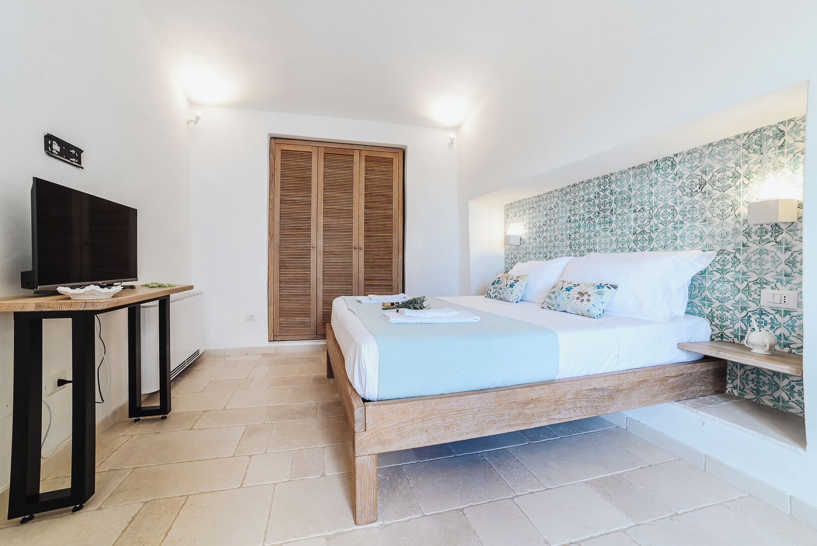 A bedroom with a bed, a TV, a wardrobe, and a wall with a patterned design.