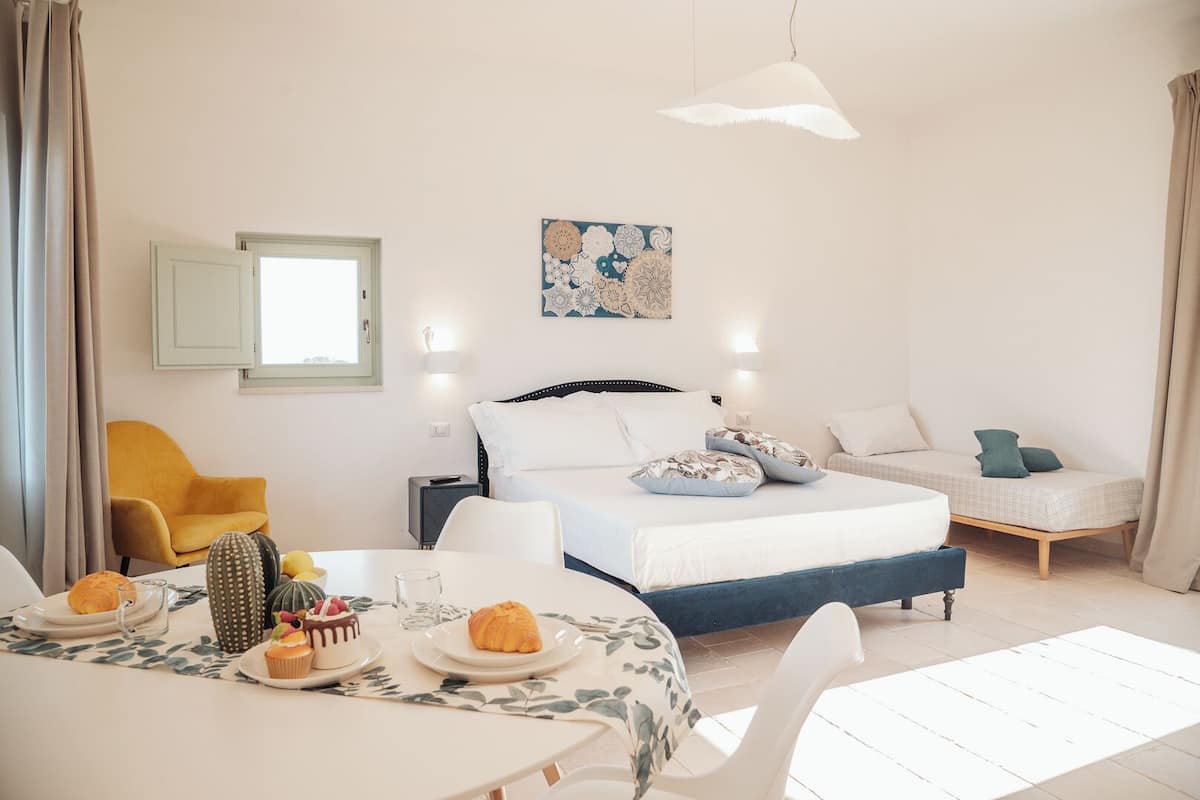 Une chambre à coucher avec un lit, des tables de chevet, une chaise, une table avec de la nourriture et une œuvre d’art murale.